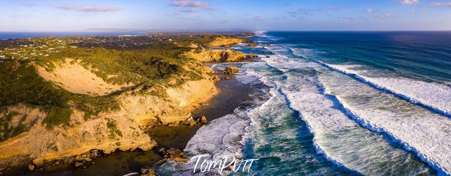 A long shot aerial view of beach connecting with a long wall of mounts having grass and bushes on them, Back Beaches Sorrento - Mornington Peninsula