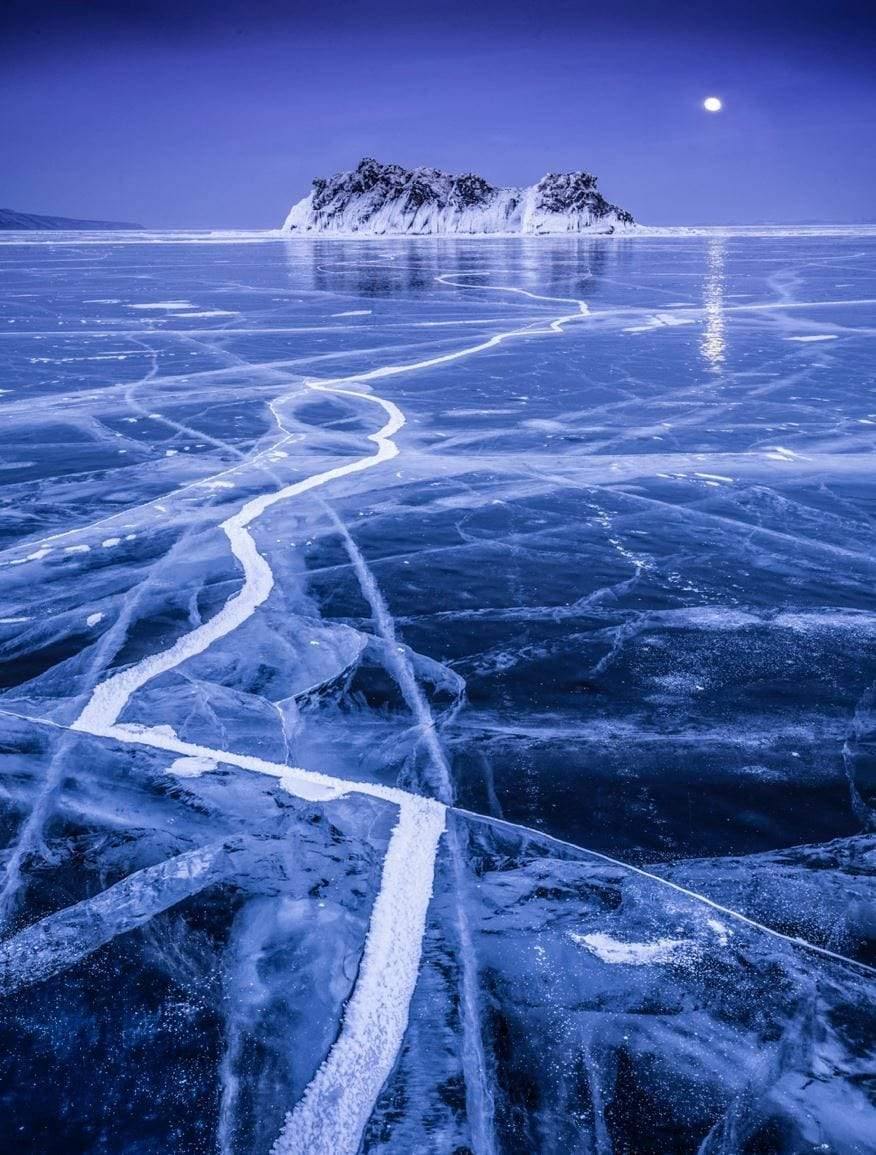 Beautiful snow ground with a lot of cracks is leading towards the snow mountain having the moon far behind it, Baikal Supermoon - Russia
