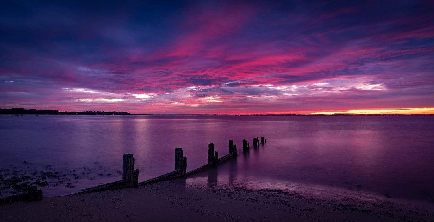 A night view of the dark purplish sea with small wood pillar series into the water, and dark purple sky with a little orange, and smoke shades, Balnarring Sunrise - Mornington Peninsula Victoria