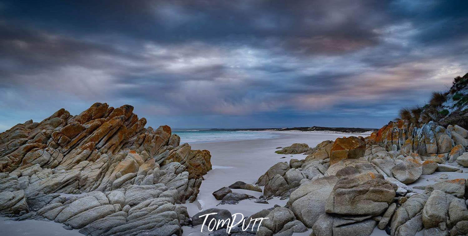 The weird shape of rocky stones on the sand of a seashore, stormy weather with dim daylight, Bay of Fires Panorama - Tasmania