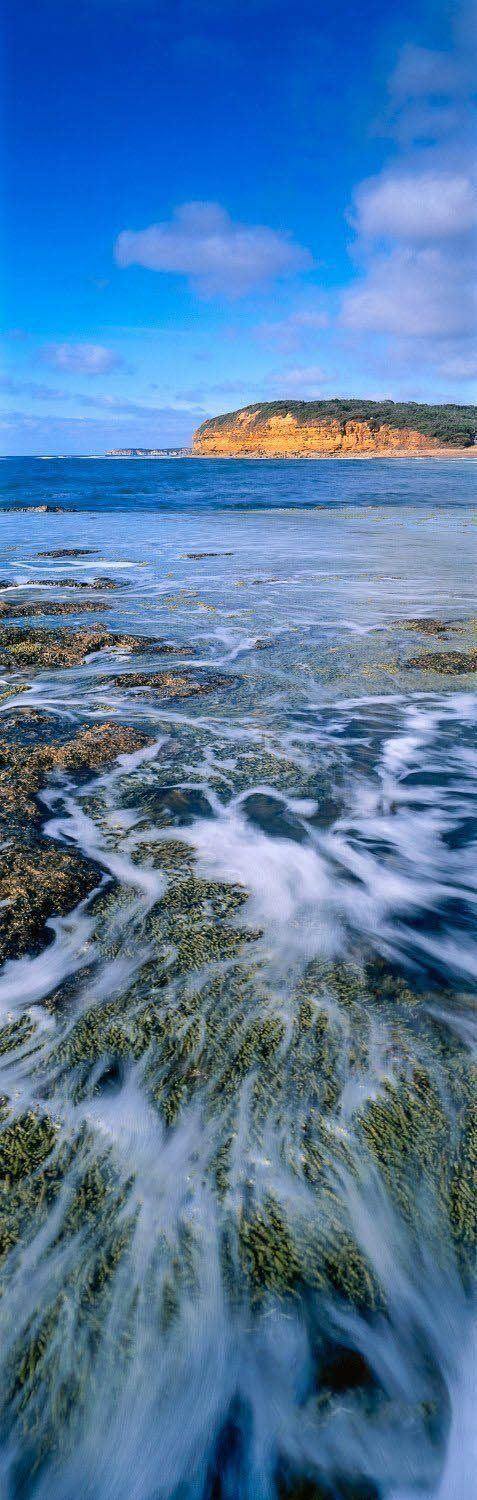 A portrait view of a beautiful sea corner with crystal clear bubbling waves, and a giant mountain wall in the far background, Bells Beach - Great Ocean Road Victoria  