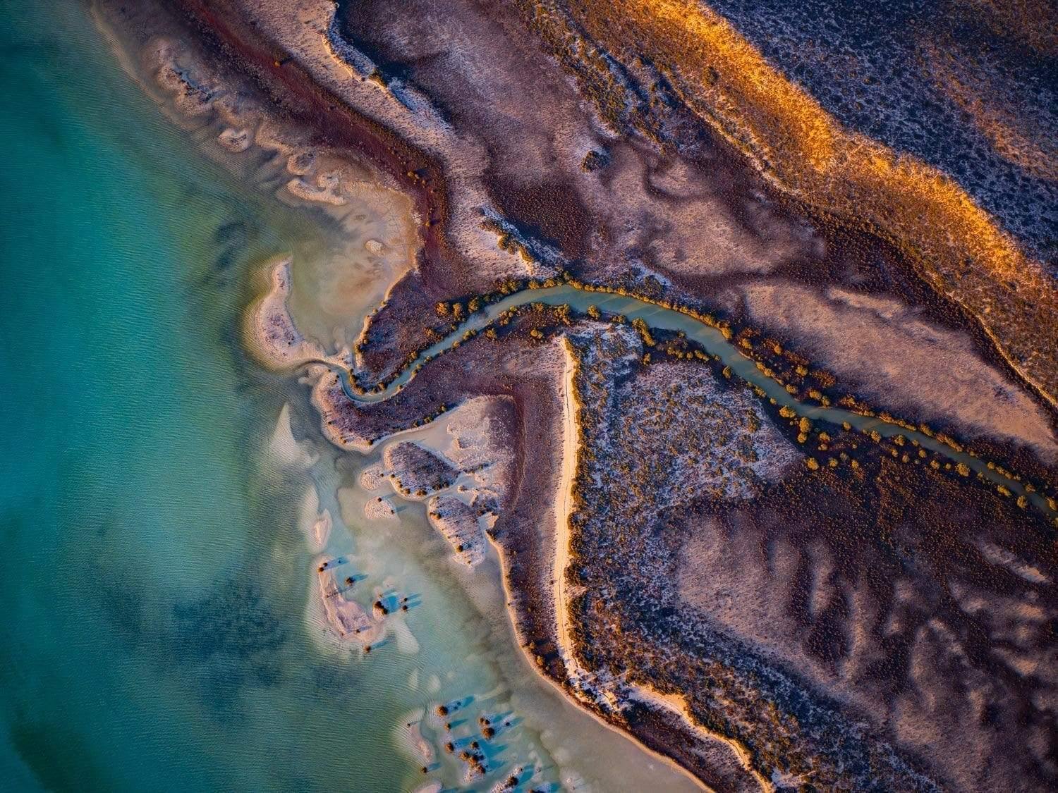An aerial view of a giant piece of the island with multi-colored sand, some trees, and a narrow water stream connecting with a sea, Blind Creek