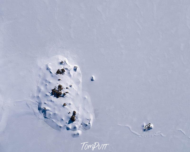 A field fully covered with the snow, an oval-shaped area with some cracks and the dark brown soil stones on it, Breaking Through Rocky Valley