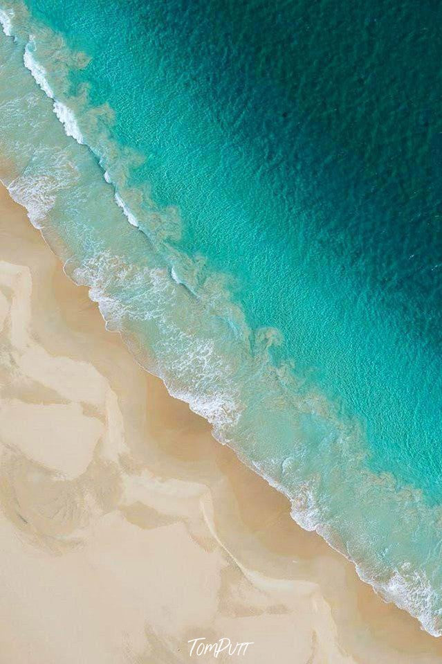 A sea-blue color ocean connecting with its shore with some lite bubbling waves, and some mustard wavy lines on the land, Bunker Bay