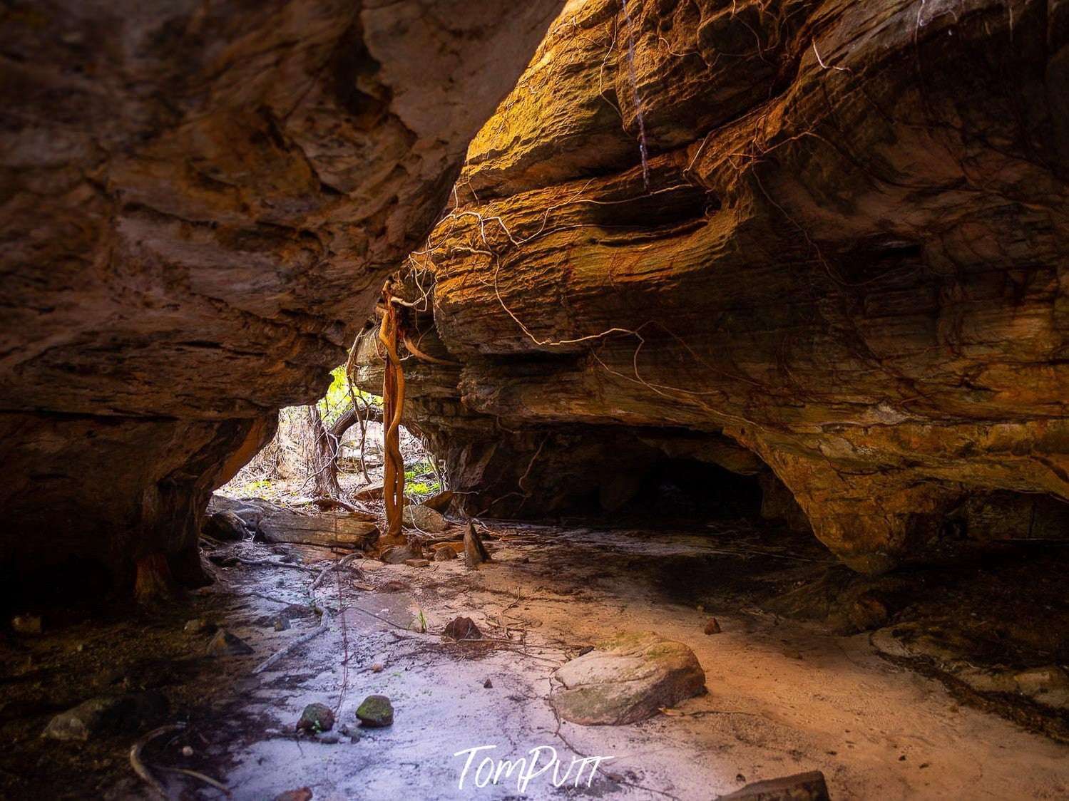 Under the giant orangish rocks, a pathway with small stones on the ground and sunlight coming, Arnhem Land 31 - Northern Territory