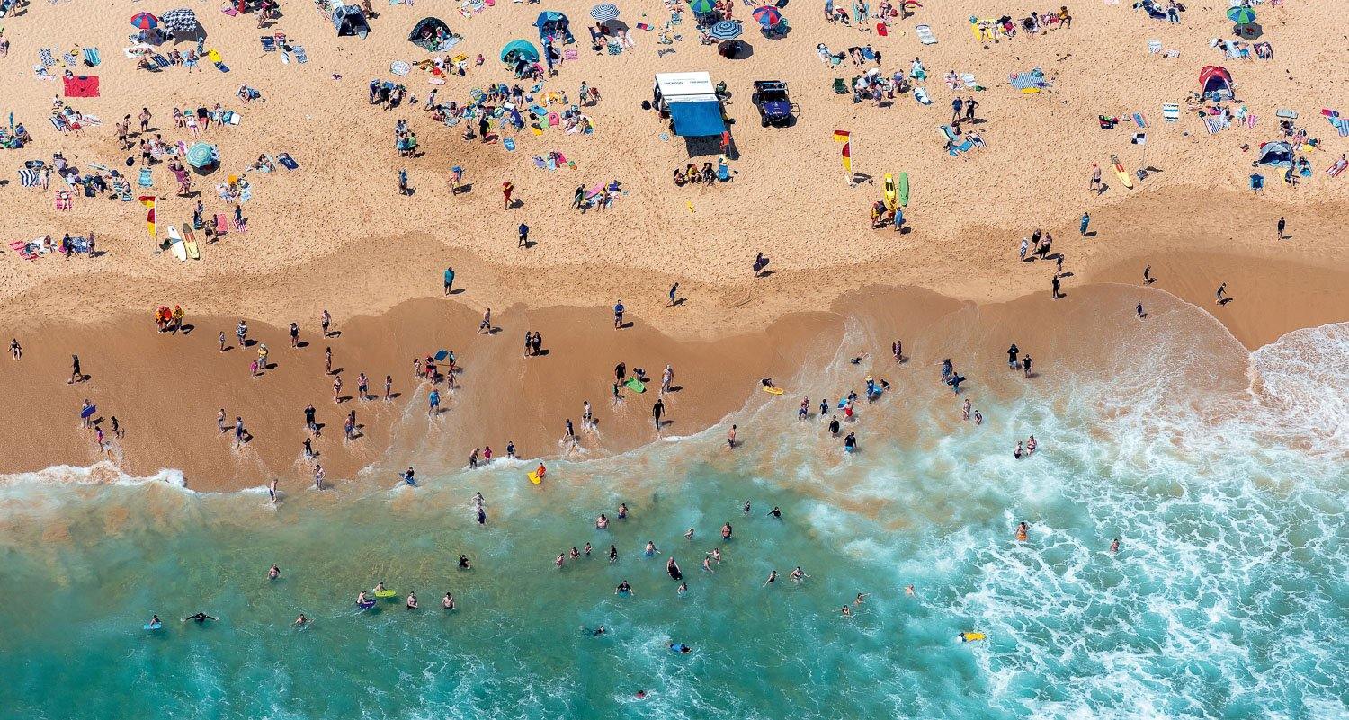 An aerial view of crystal clear water at the seashore with a lot of people in the water and on the sand, Cooling Off, Gunnamatta - Mornington Peninsula Victoria 