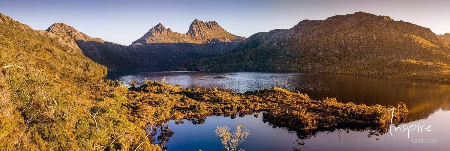 A morning view of a lake covered with green mounds and rocks with sunlight hitting on the scene, Cradle Fall - Cradle Mountain, TAS