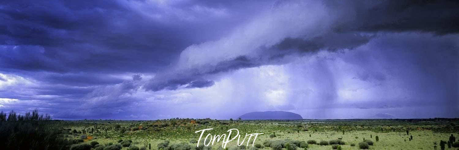 A wide greenfield area with a lot of grass, bushes, and plants, and stormy weather with dark dense clouds over the field, Desert Storm - Uluru Northern Territory