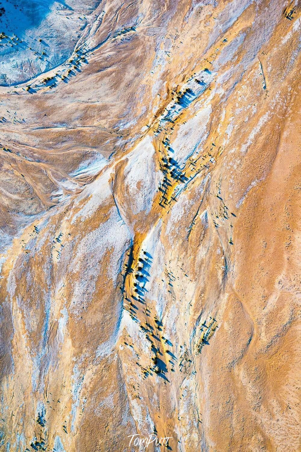 Huge desert-like land with some random lines and curves over, forming a powder and sand color combination with some small green spots, Drought