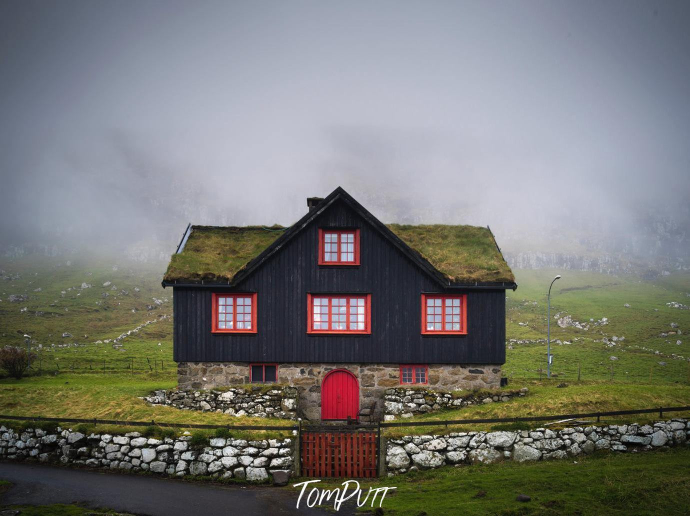 A beautiful house of black color with red outlines of windows, and a grassy roof, A greenfield area with nothing but a foggy effect in the background, Faroes Islands House
