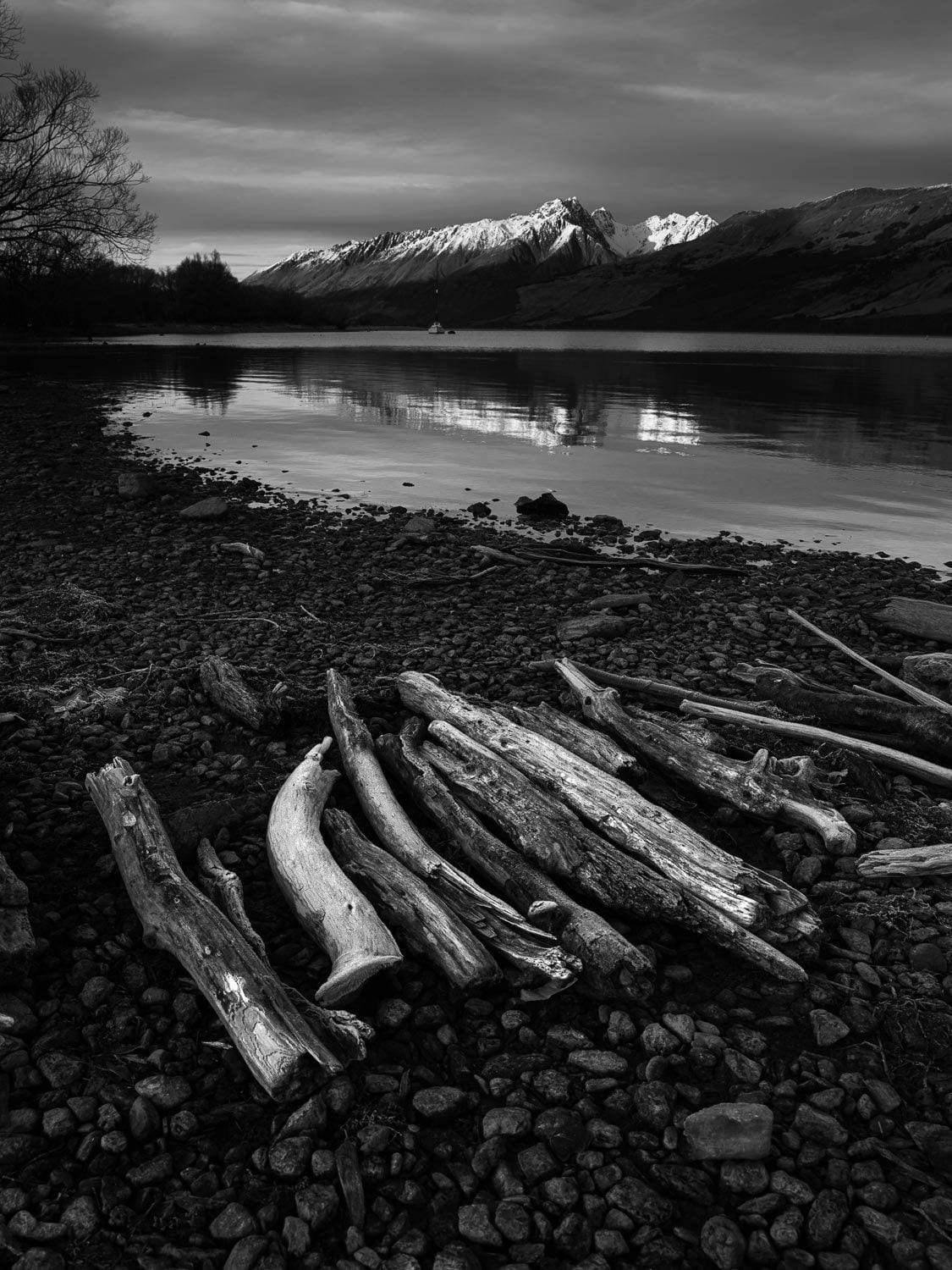 Dark view of a lake, some long wood pillar, and a mountain wall in the background, Glenorchy Shoreline - New Zealand