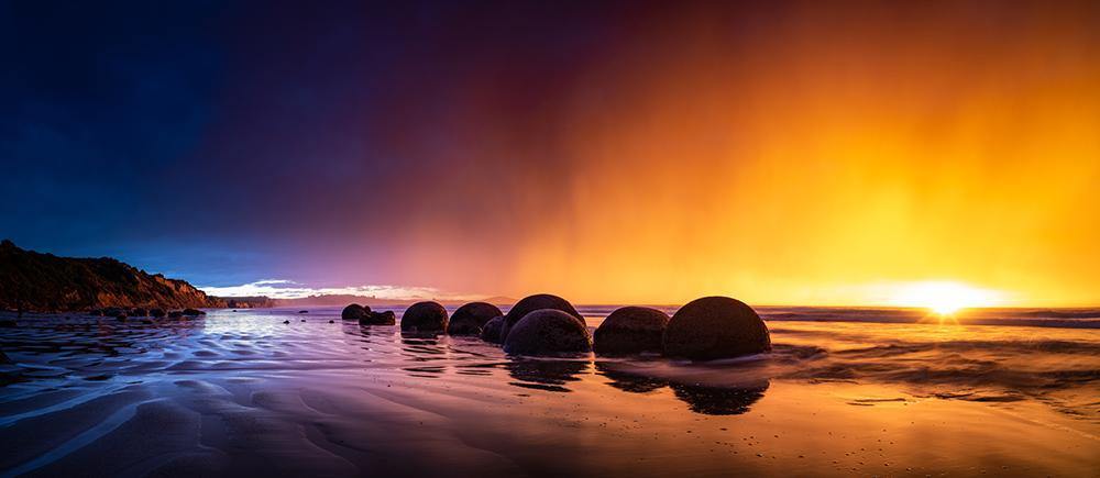 A yellow and purplish effect of sunset on a beach with a row of rounded stones, Golden Dawn, Moeraki Boulders