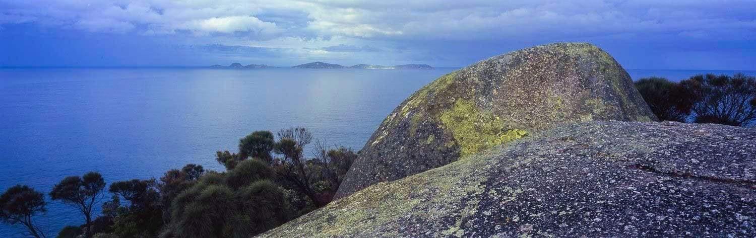 A hill area with big stones, some trees and a beach in the background, Granite Island - Wilson's Promontory VIC