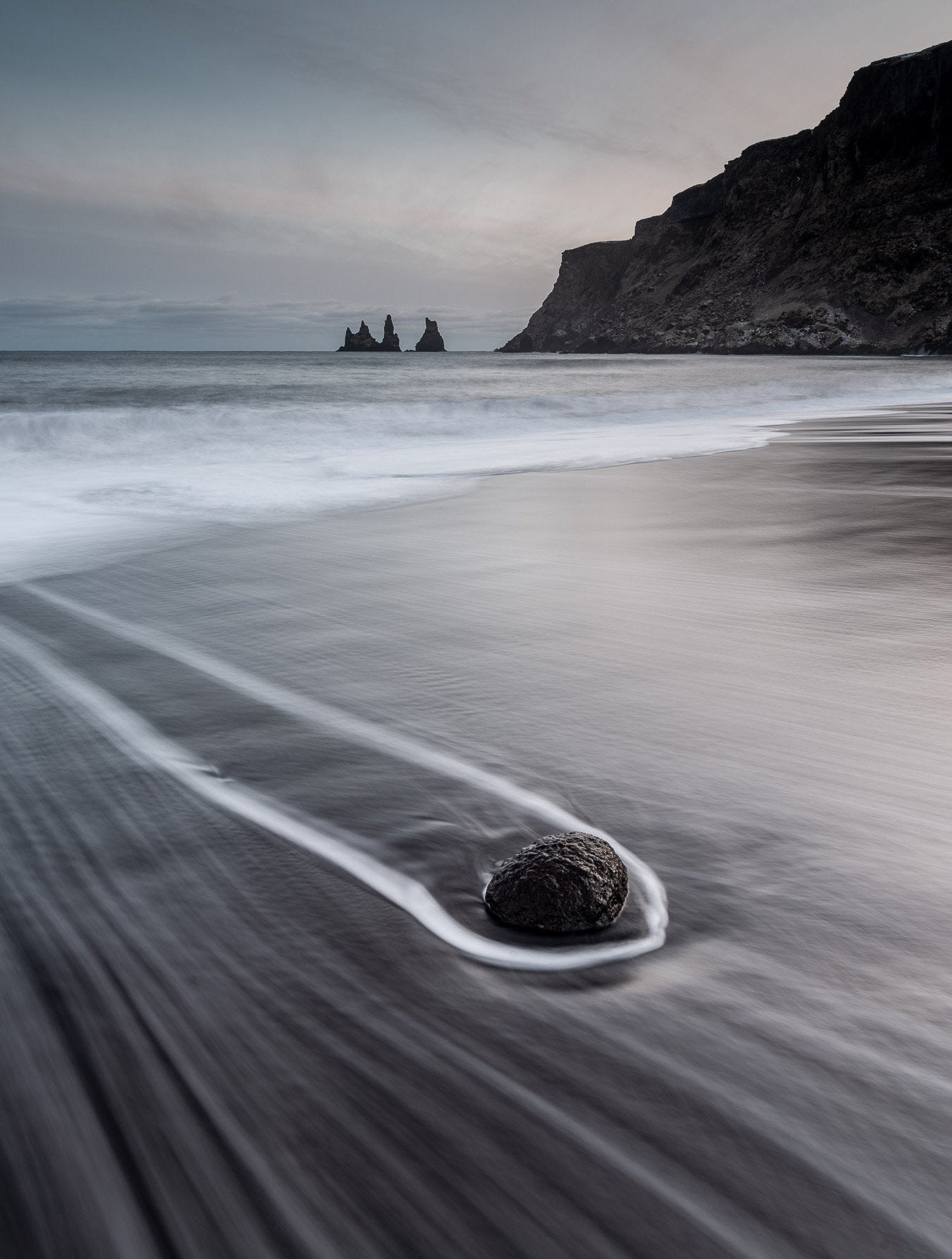 A dark view of a beach with a rounded stone dragging, and a giant mountain in the background, Iceland #22