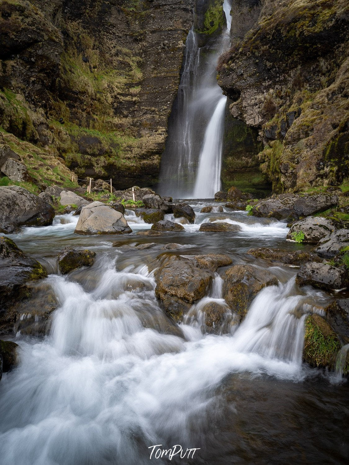 A beautiful waterfall coming from a hill area of a tall mountain wall, making a watercourse on the land, Iceland No.33