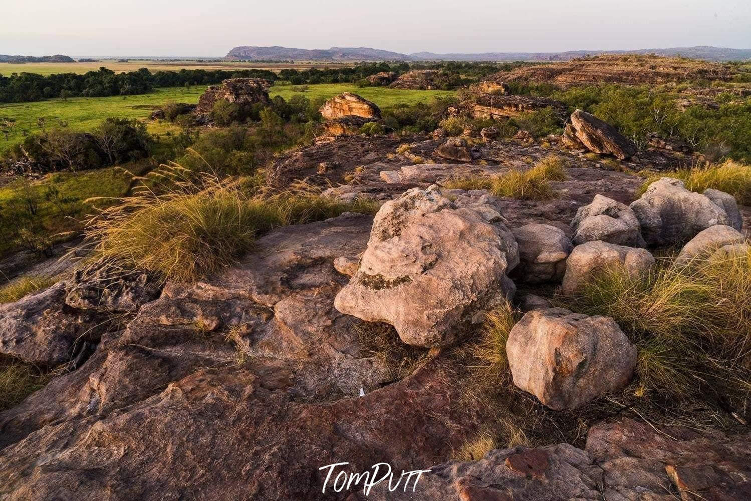 A rocky land with some stones, and a long greenfield area in the background, Kakadu Territory - Northern Territory