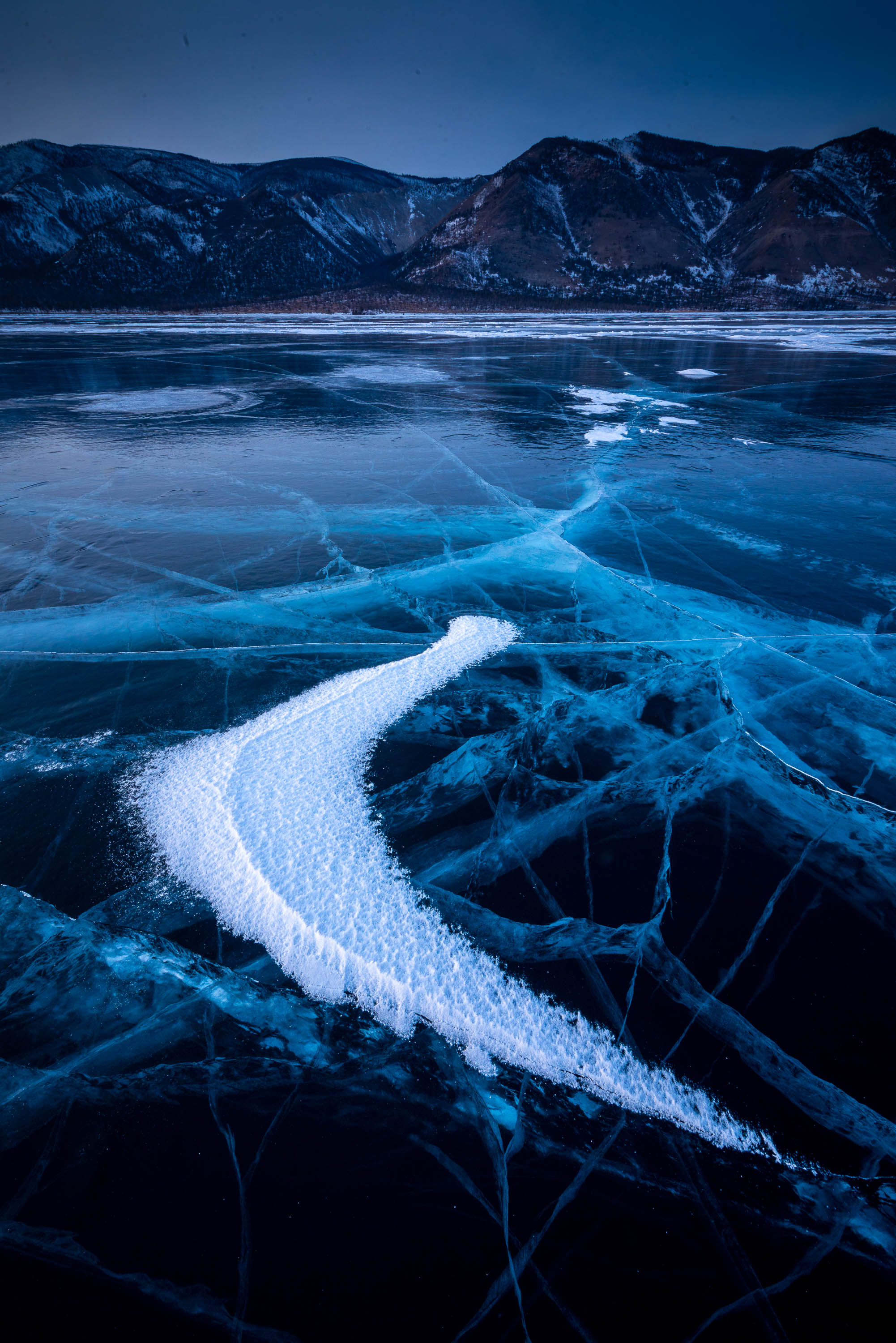 A frozen lake with some fresh snow, and a long mountain wall in the background, Lake Baikal #30, Siberia, Russia