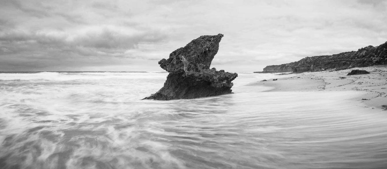 Black and white picture of a large mountain standing in the middle of a sea, Lizard Rock, Rye - Mornington Peninsula VIC
