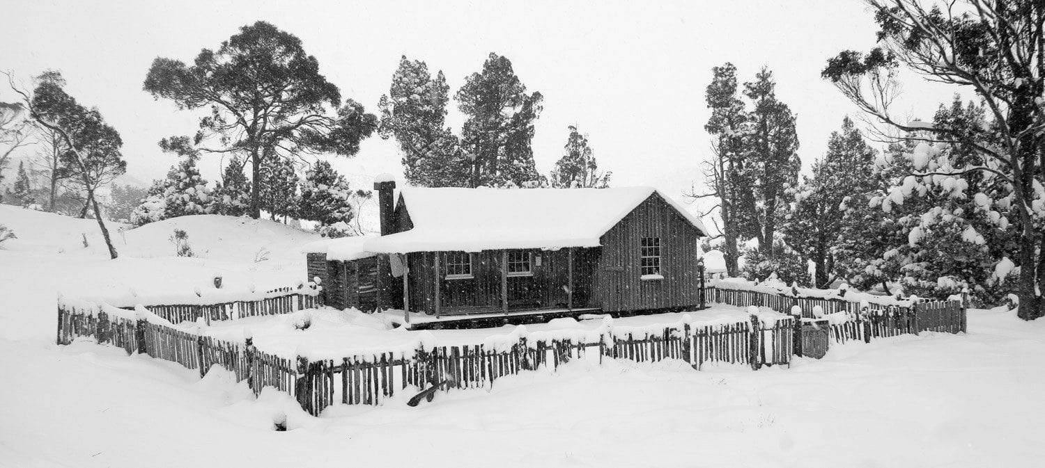 A house with a fence and some trees around, fully covered with snow, Mount Kate Hut - Cradle Mountain TAS