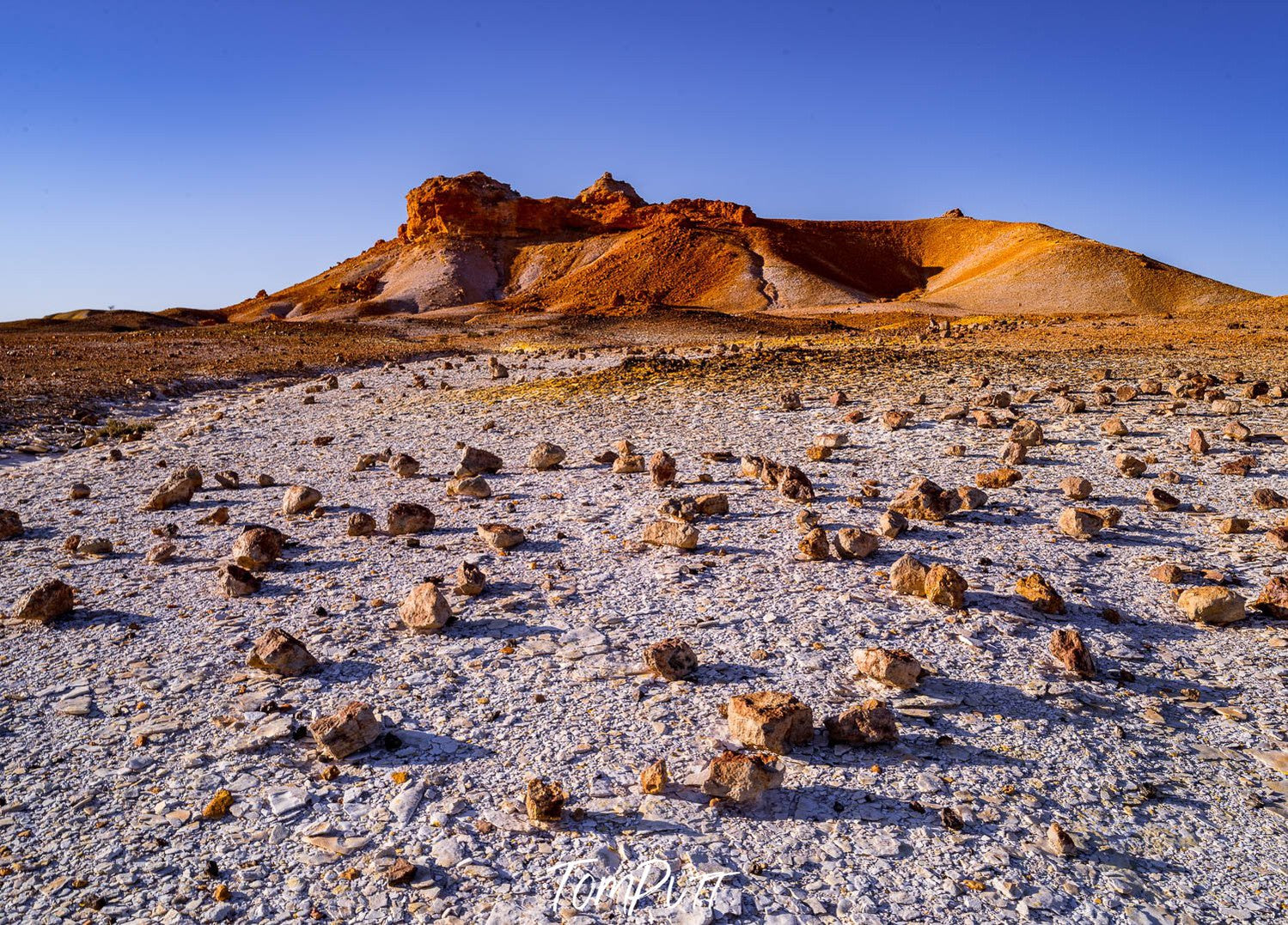 A cracky surface with small stones on the ground following a mountain wall with a high mound, Painted Hills #33