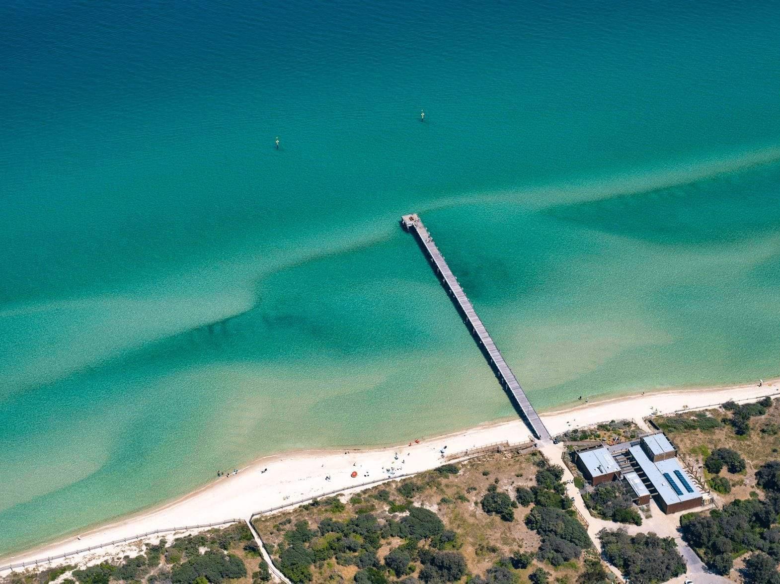 Aerial view of a seashore with a long and narrow bridge over, Seaford Pier from above, Mornington Peninsula, Victoria
