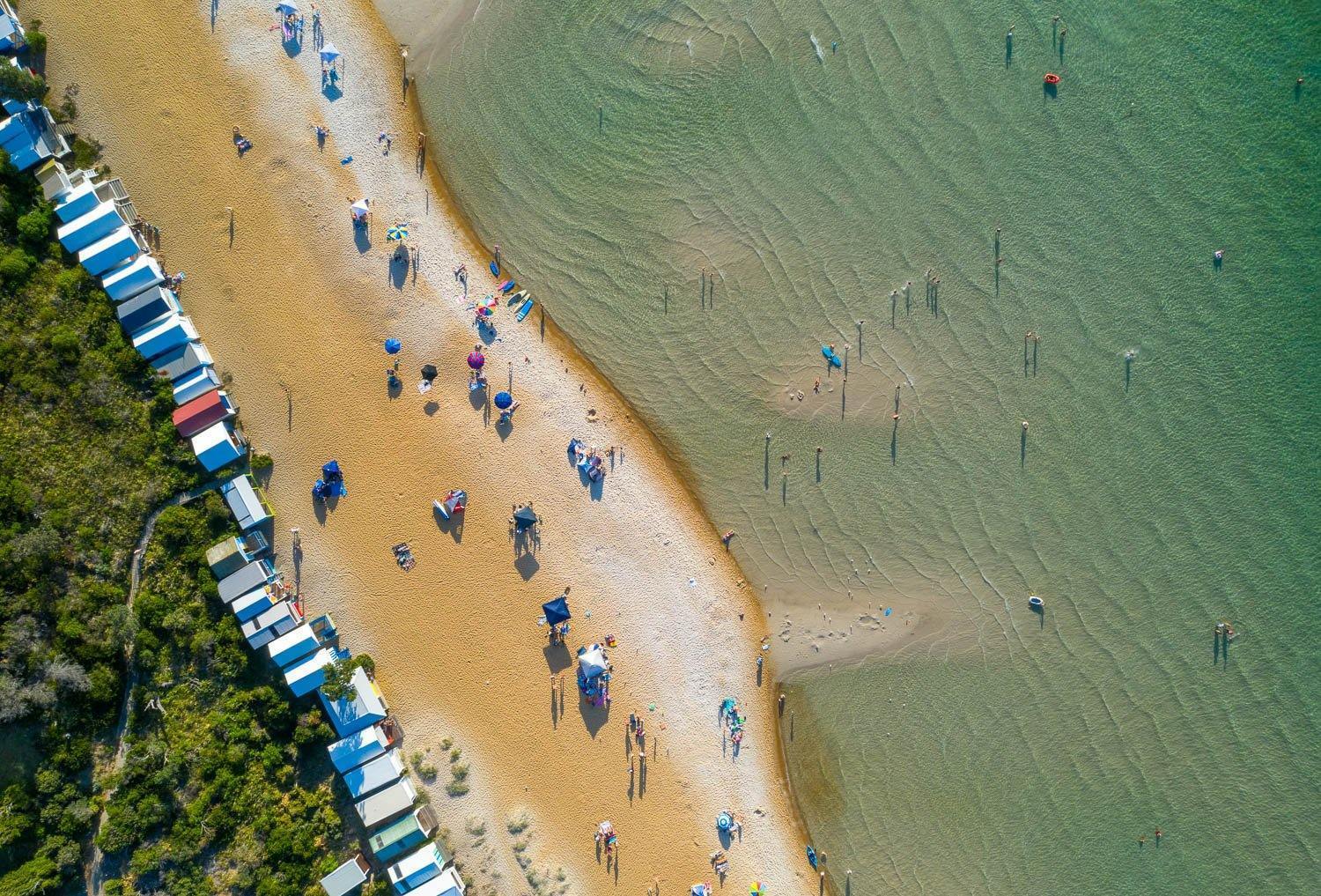 Aerial view of a calm beach with some people and colorful huts outside, Summer Bathers Mt Martha - Mornington Peninsula VIC