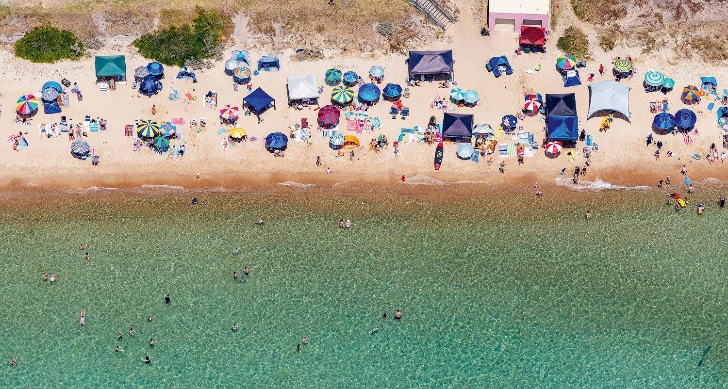Aerial view of a beautiful green beach with many people and huts, Summer Solstice - Mornington Peninsula VIC