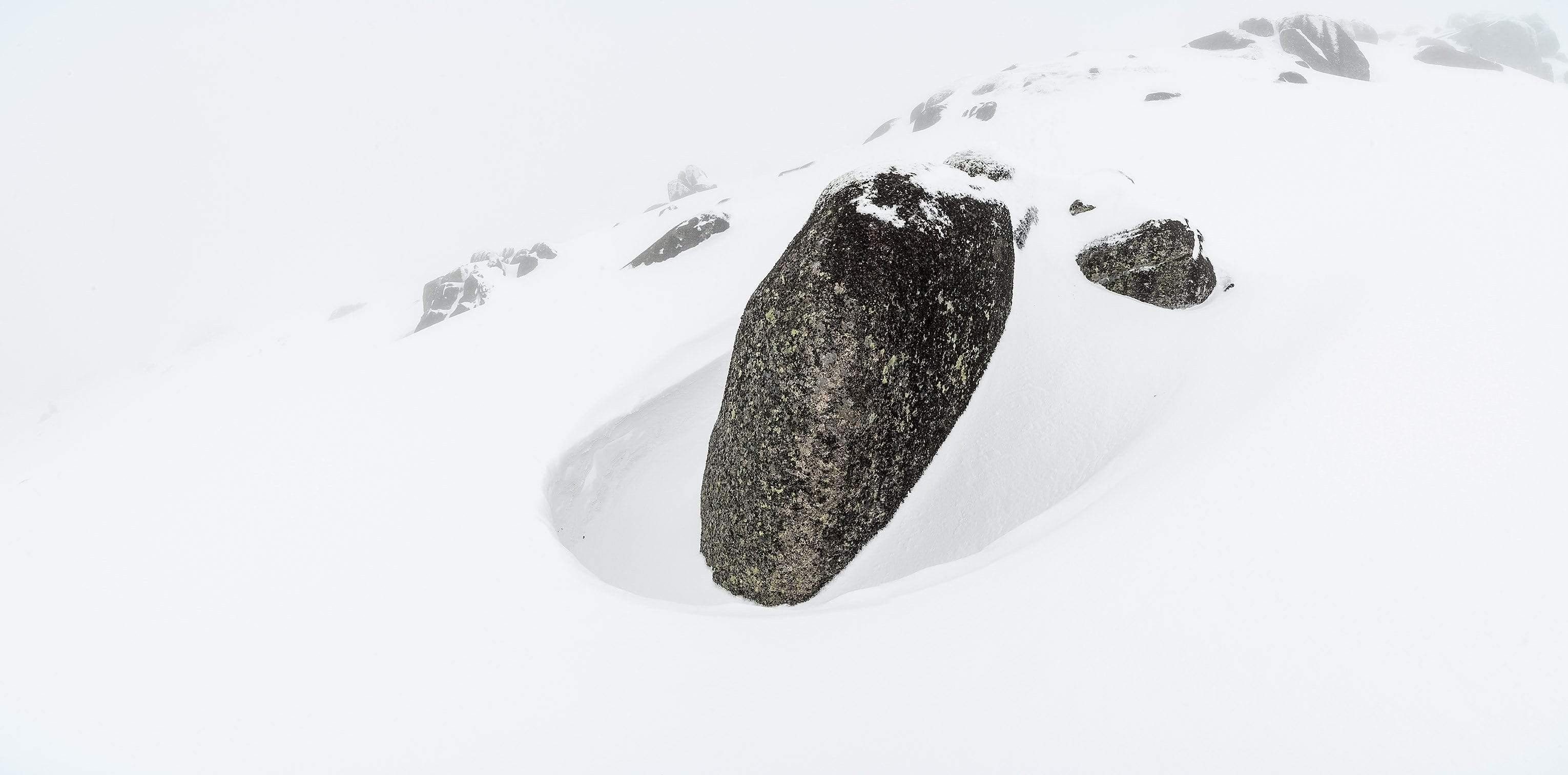 A fully white snow-covered land with a black stony rock, Teardrop - Snowy Mountains NSW