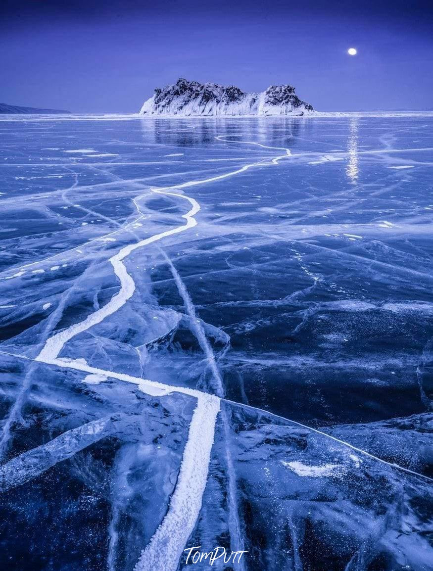 Beautiful snow ground with a lot of cracks is leading towards the snow mountain having the moon far behind it, Baikal Supermoon - Russia