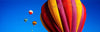 A giant colorful balloon in the air with some small similar balloons in the background, Balloons Aloft