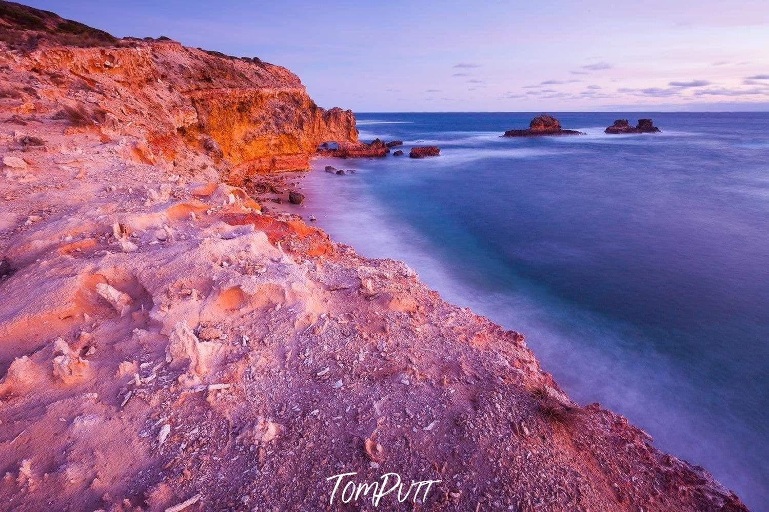 A morning view of a giant mountain wall with a seashore connecting to it, some big mounts are standing in the water in the far background, Bay of islands - Mornington Peninsula Victoria 