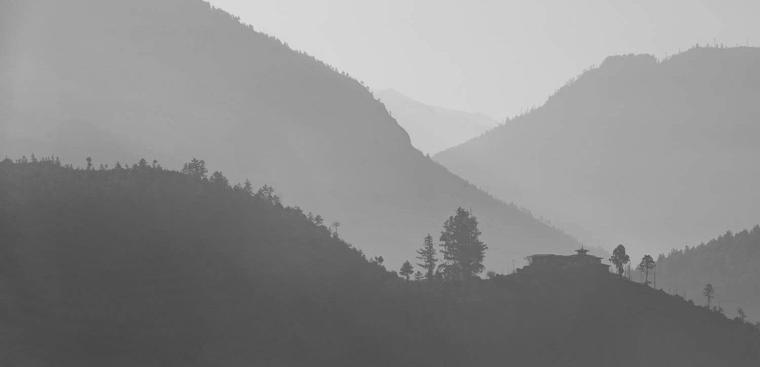 A black and white view of a dull smoky evening with great grassy mountains and some trees on them, Bhutan Countryside