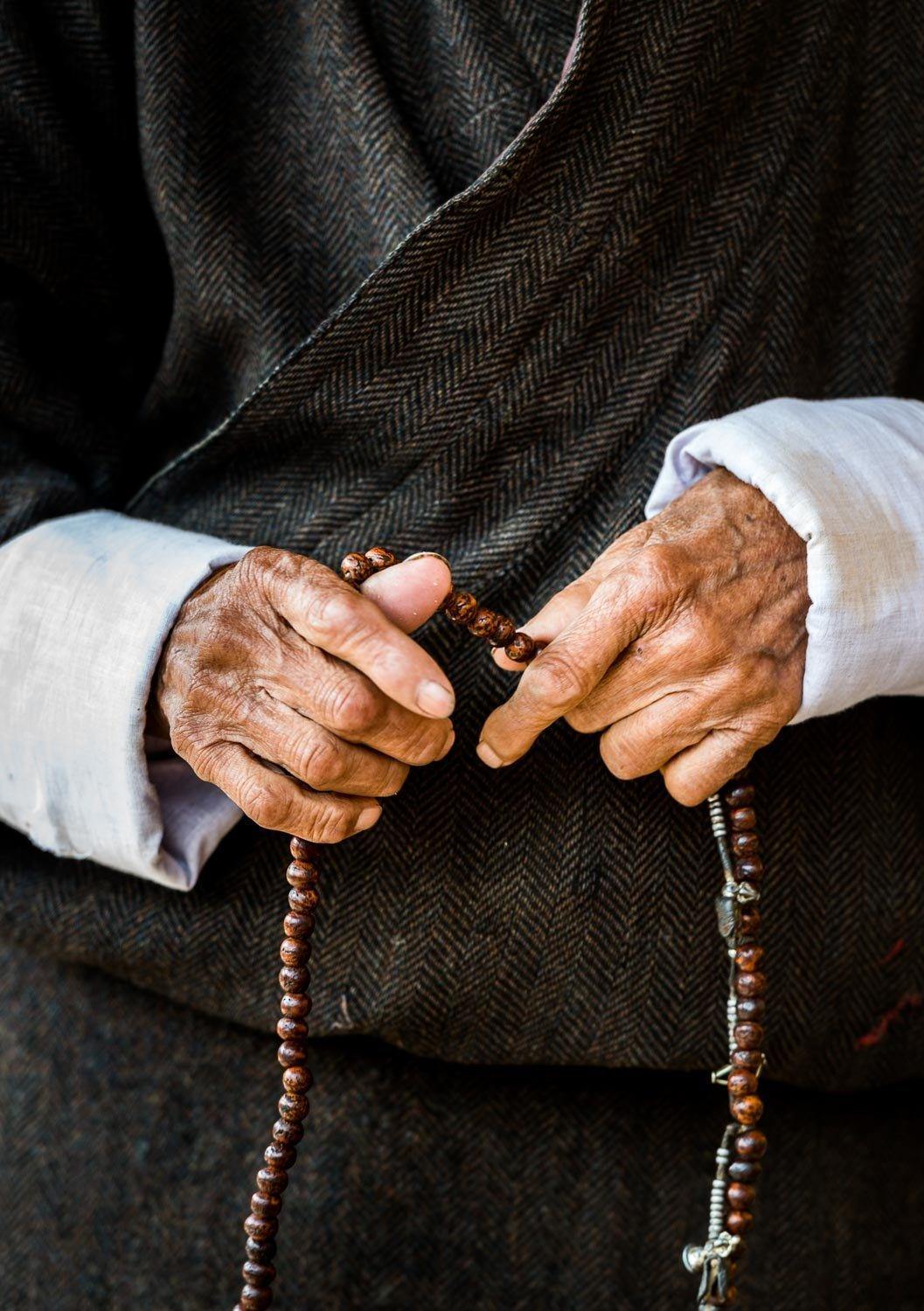 A close-up shot of an old human's hand holding prayer beads and wearing a black gown with white sleeves, Bhutan prayer beads