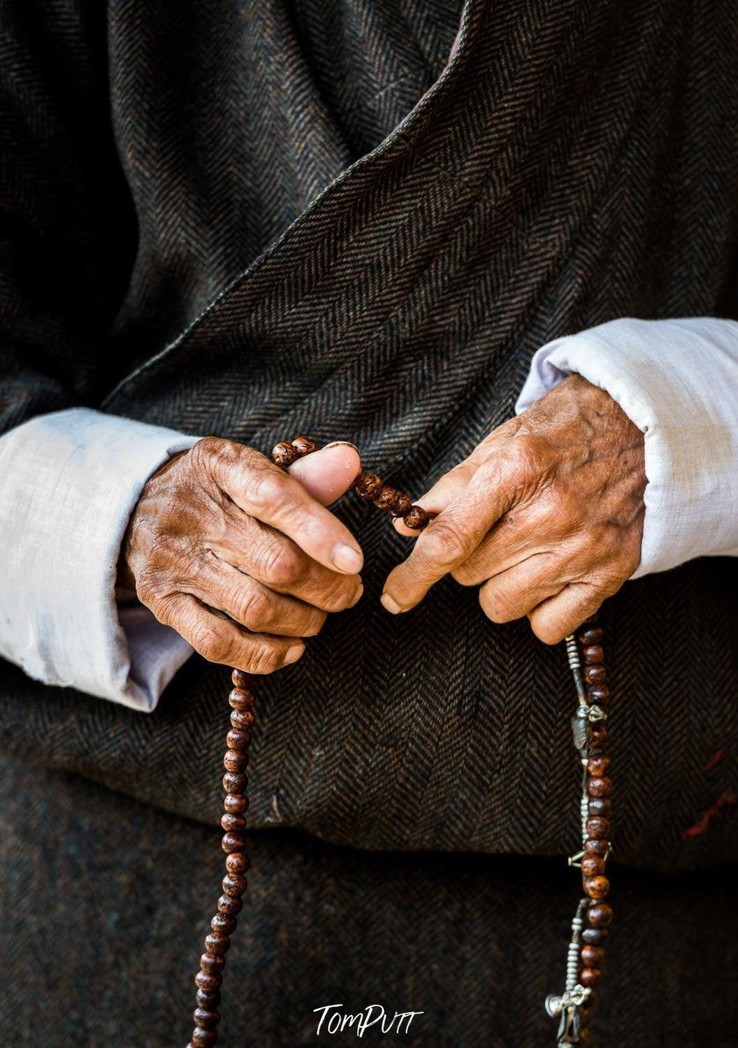 A close-up shot of an old human's hand holding prayer beads and wearing a black gown with white sleeves, Bhutan prayer beads