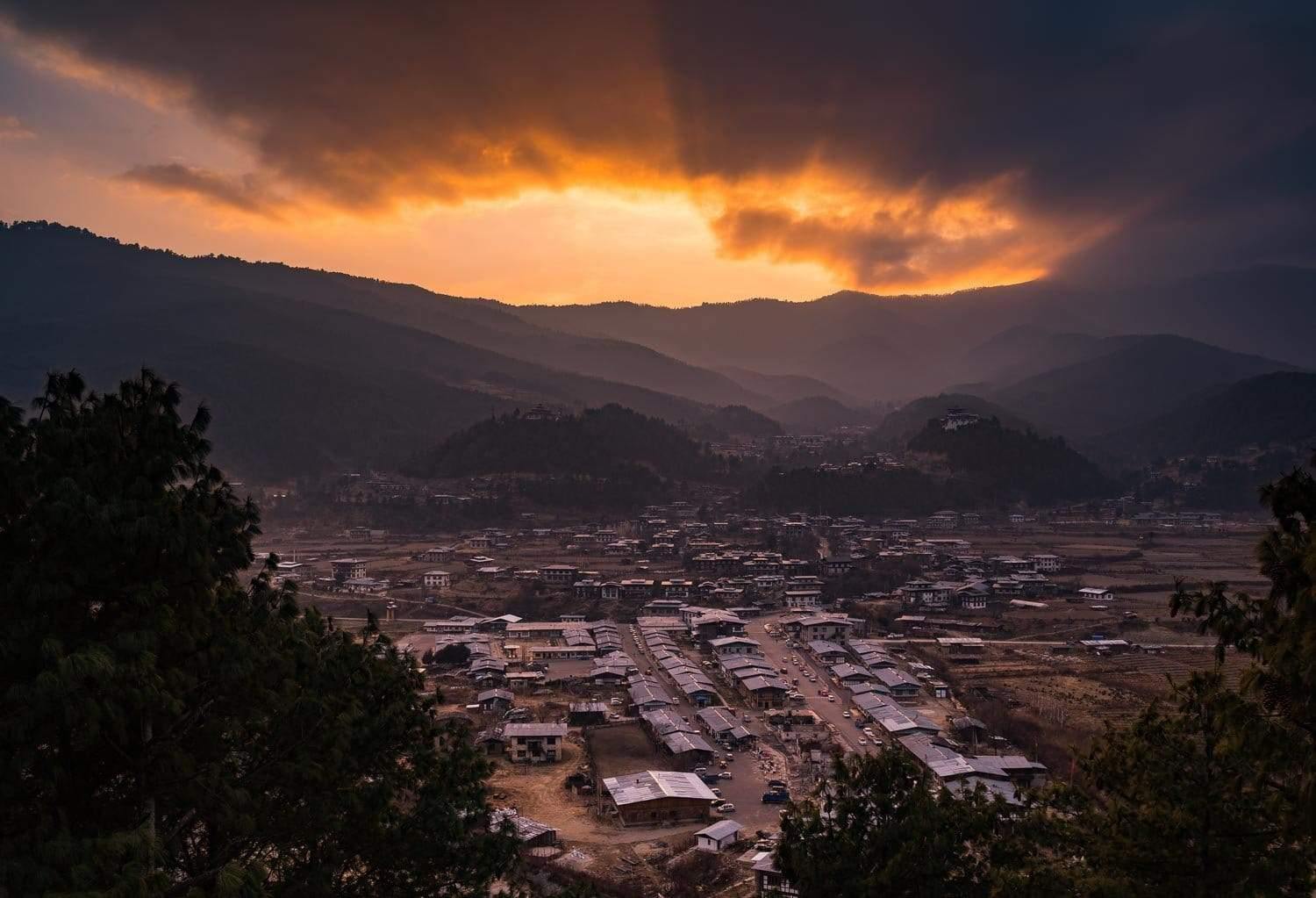 A long-shot view of sunset in a beautiful village surrounded by mountains wall, and the trees windowing the entire scene, Bhutan Sunset