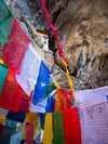 A close-up view of a series of colorful prayer flags and a prayer place on the rock in the near background, Bhutan Temple and Prayer Flags