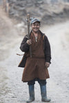 A smiling mid-aged man with a long-handled axe in his hand, wearing long black shoes and a brown traditional gown, Bhutan Tradesman