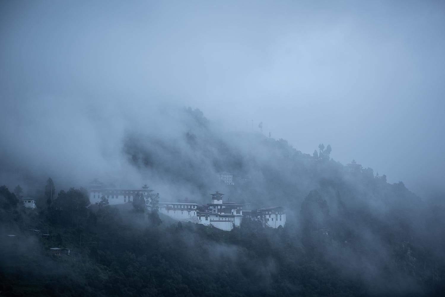 A fort on the edge of the hills with high mountains and greenery around it, and some great smoke effect on the entire picture, Bhutan Zhong
