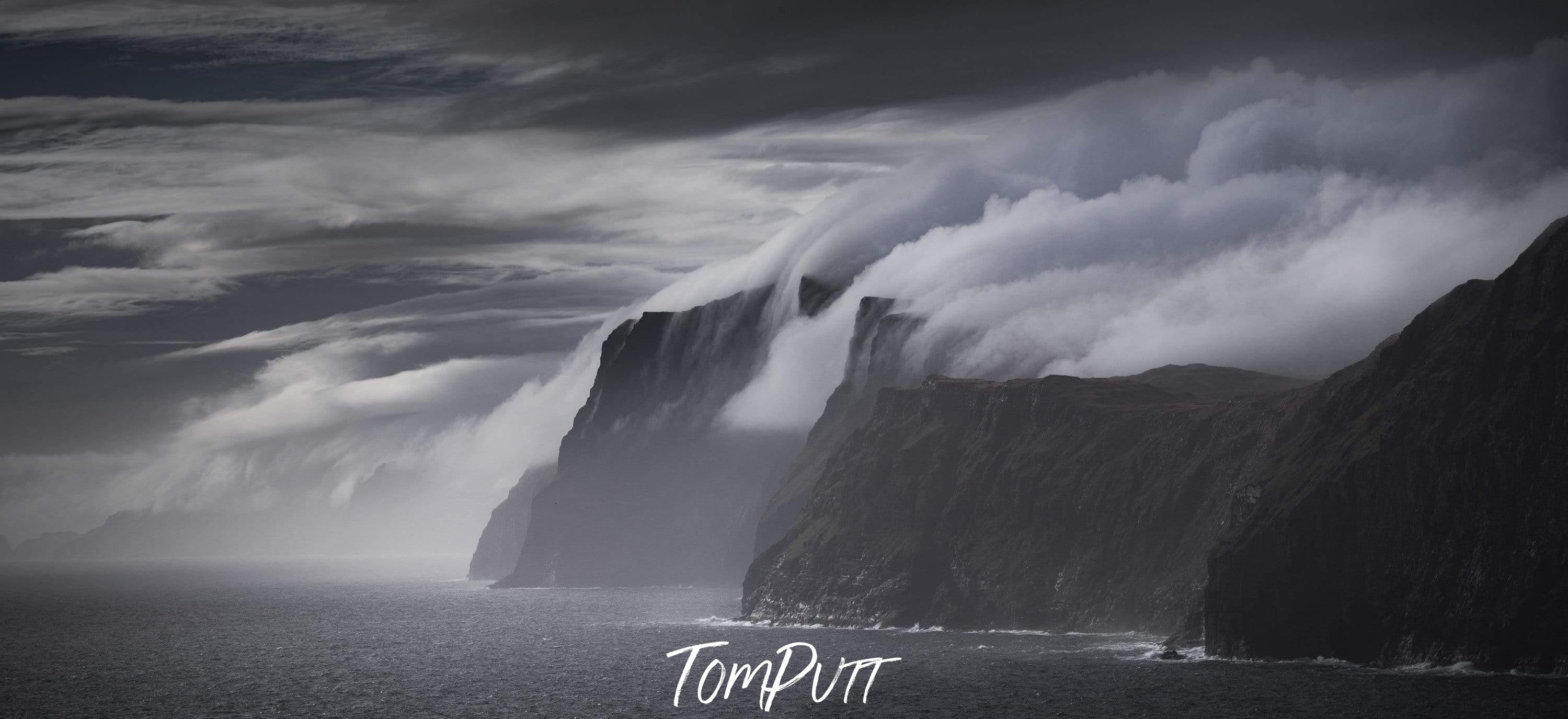 Giant black mountains in the sea with heavy smoky clouds over them, a breathtaking view of an evening dim light, Blowing Over, Faroe Islands