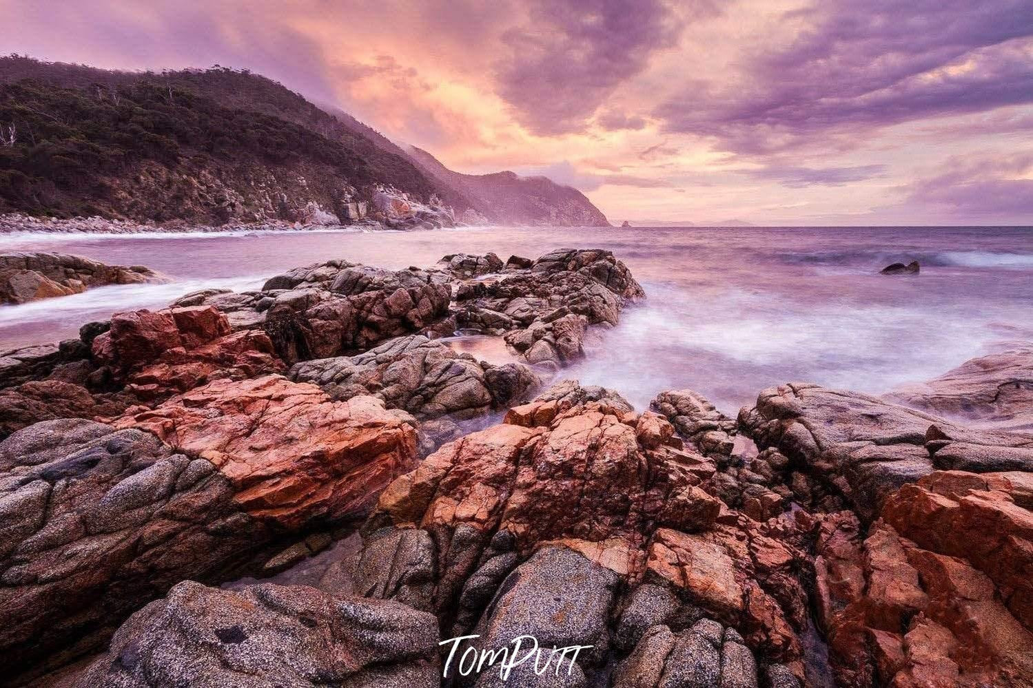 A series of gapless cracked stones on the seashore with a long mountain wall covered with grass on the left top corner, Bluestone Bay - Freycinet, TAS