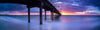 A dim light early morning view of an over-water bridge with its pillars in the water, and a purplish and blue shade on the sky with a little sunlight spreading in the far backgkround, Brighton Jetty - Adelaide SA
