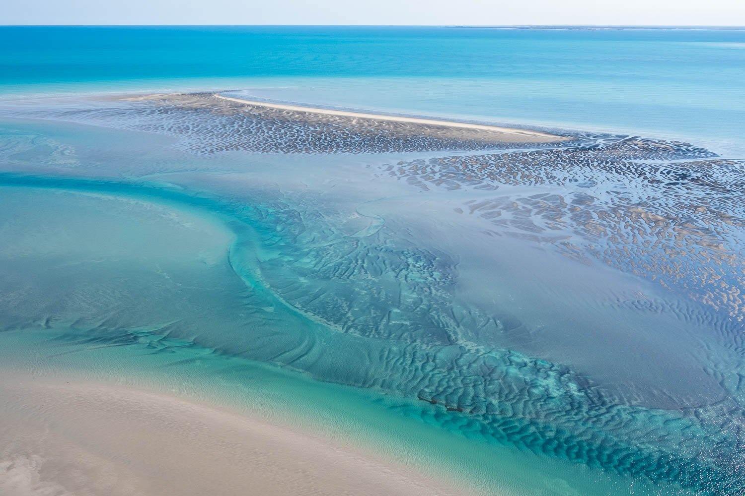 A wide oceanic area with a multi-colored pattern of water and some stone wall underwater, Broome #19