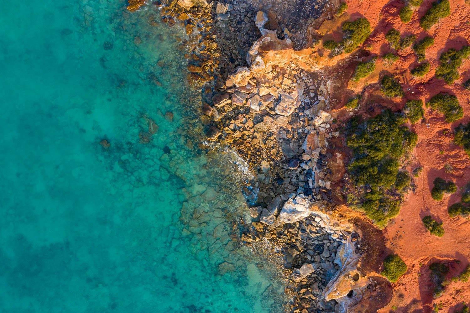 A long-shot aerial view of a lake corner with a lot of rocky stones, and an effect of the early sunlight falling on the scene, Broome #29