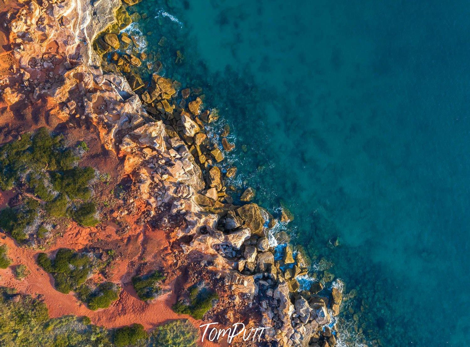 A long-shot An aerial view of a lake corner with a lot of rocky stones, some sand and greenery beside the stones, and an effect of the early sunlight falling on the scene, Broome No.30