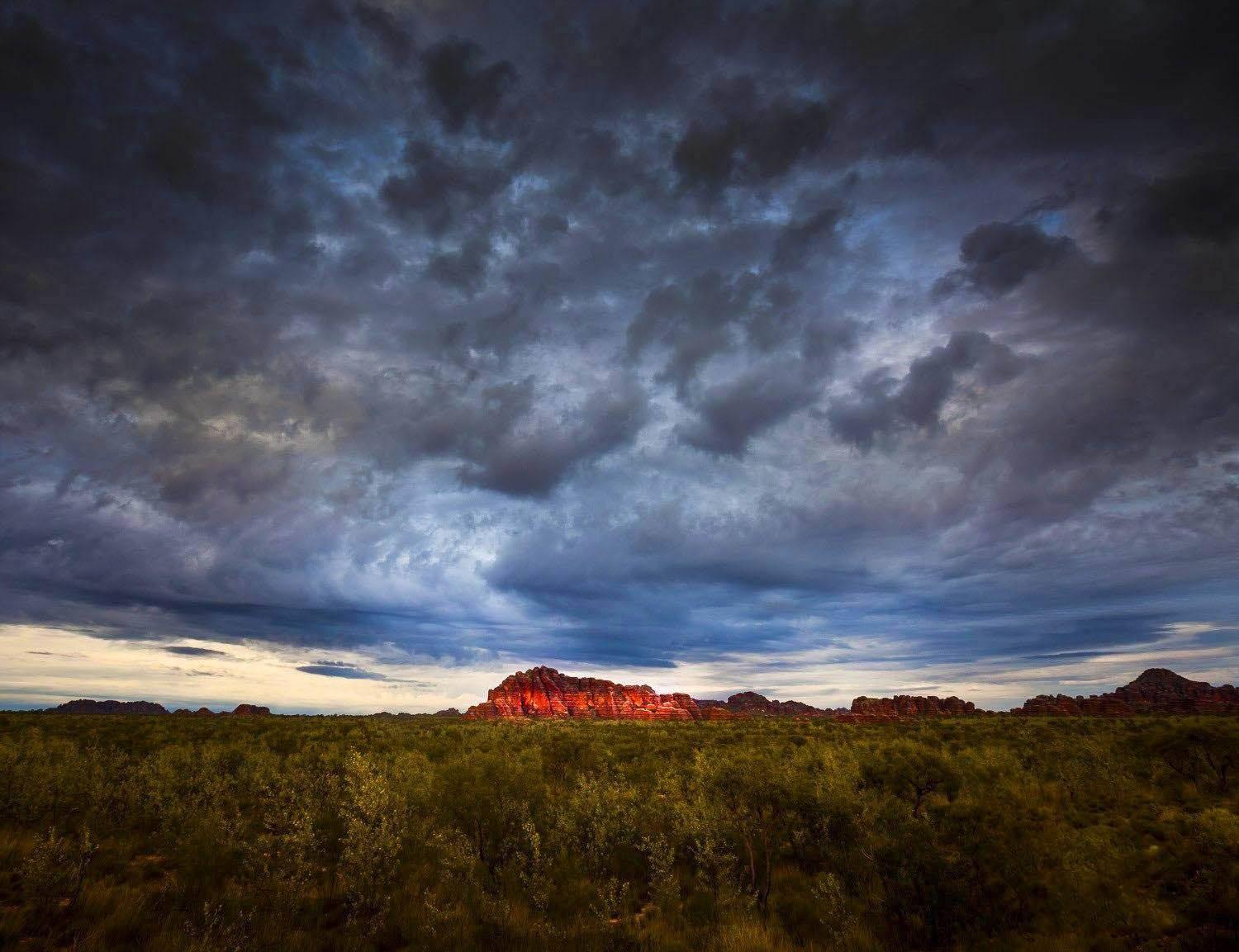 The great mountain wall with a giant black dense cloud over it, and a lush green field in the foreground, Bungle Bungle Storm - Purnululu Bungle Bungles