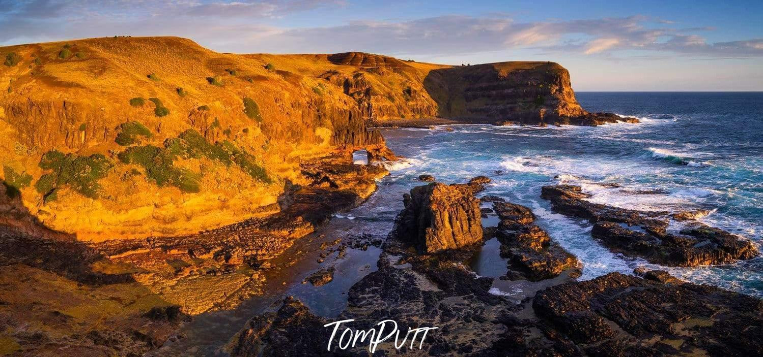 A long wall of giant mountains with a sea connecting, and a yellowish effect of sunlight hitting on the scene, Bushrangers Gold - Mornington Peninsula