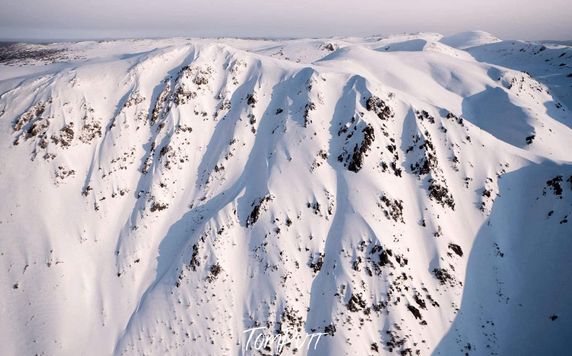 A giant mountain fully covered with fresh snow and some spots of wet sand on it, depicting a white ice-cream with chocolate chips on it, Carruthers - Snowy Mountains NSW