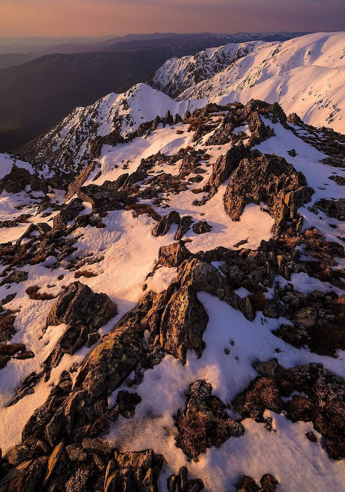 A giant mountain wall fully covered with fresh snow and some spots of wet sand on it, depicting a white ice-cream with chocolate chips on it, Carruthers Sunset - Snowy Mountains, NSW