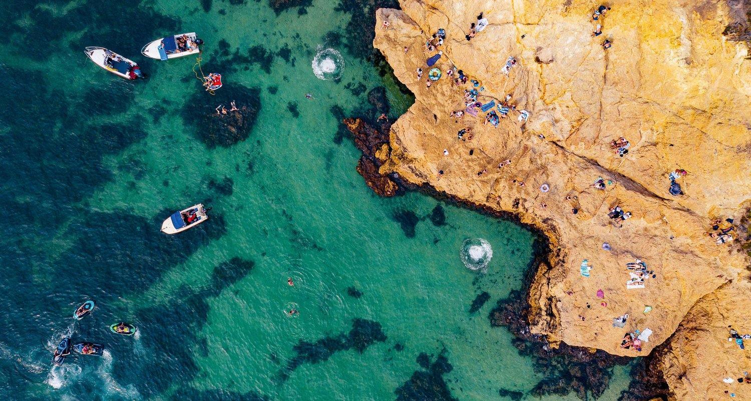 a deep sea-green color ocean having some boats in it with a giant rock serving as a beach for people, Circular Splashes - Mornington Peninsula