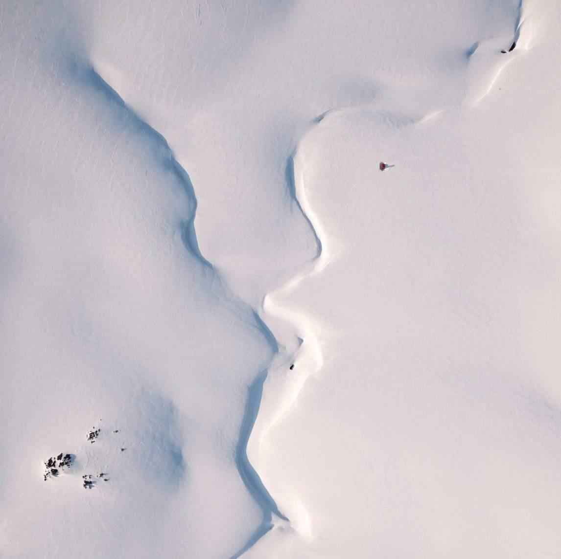 An aerial view of a snow-covered area forming a convergence in the middle, and some small black spots in the left bottom corner, Convergence - Snowy Mountains New South Wales    